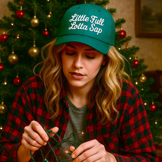 Woman wearing a green cap with 'Little Full Lotta Sap' text, sitting in front of a decorated Christmas tree.
